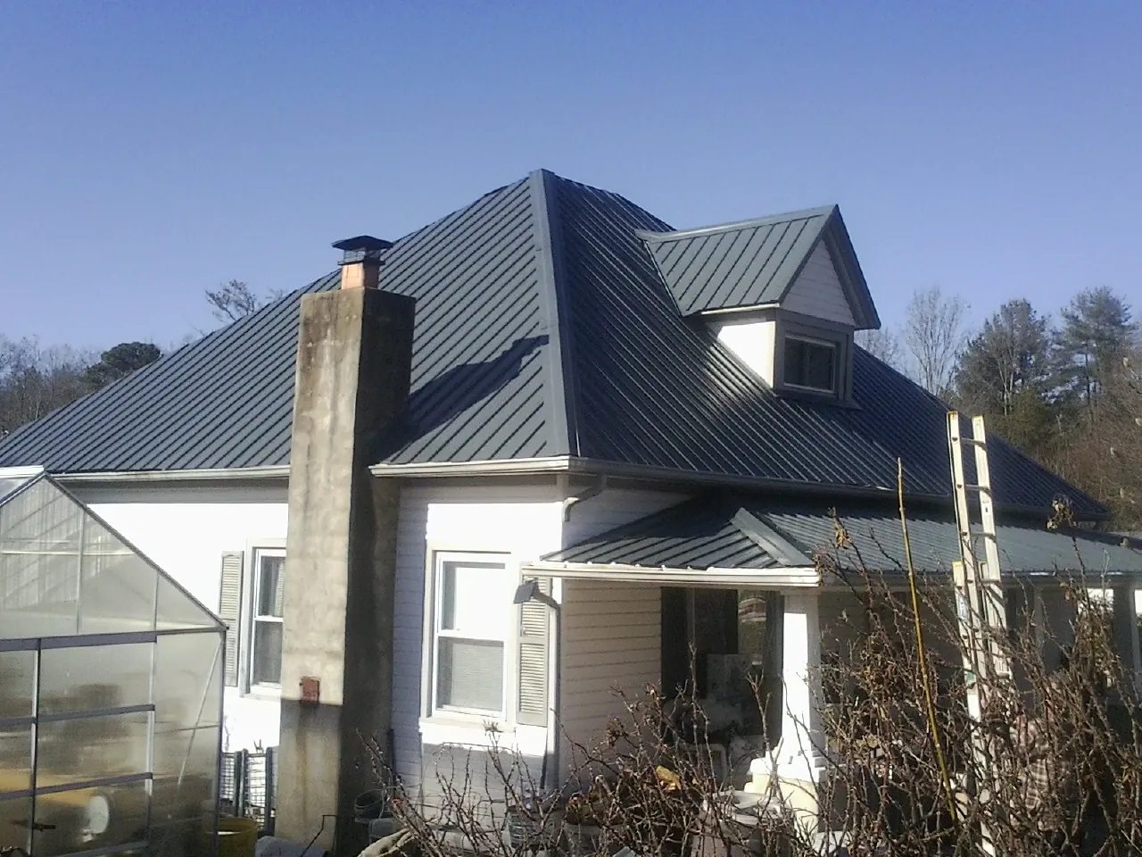 Dark blue standing seam metal roof on a white farmhouse with dormer — Slate & Tile Roof Repair by Roofing Brothers in Omega