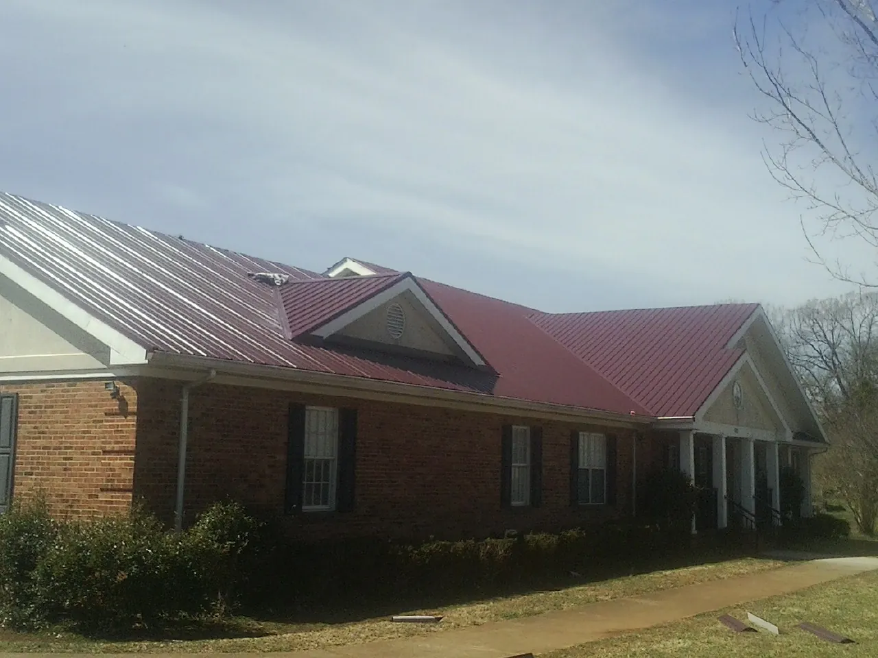 Red metal roof with gabled entries on a long brick building, from a Hail Damage Roof Repair job in Omega