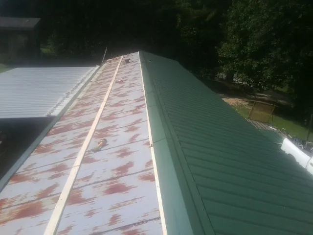 Old rusted panels beside newly installed green metal roofing — Wind Damage Roof Repair by Roofing Brothers in Omega