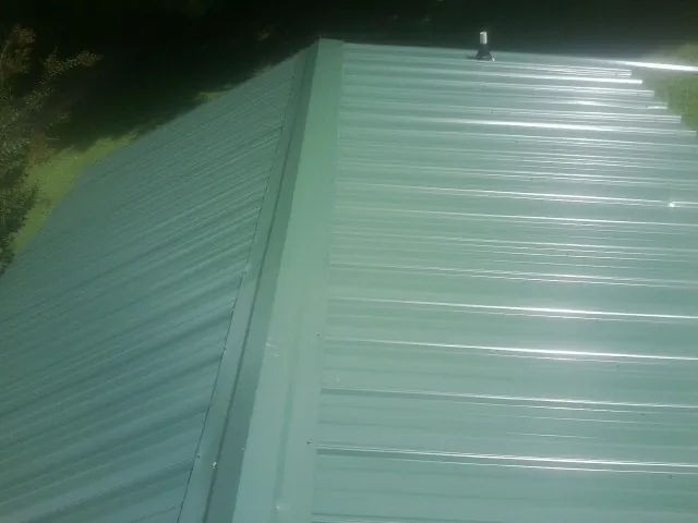 New green metal panels meeting at the ridge of a roof — Flat Roof Repair work by our crew in Omega
