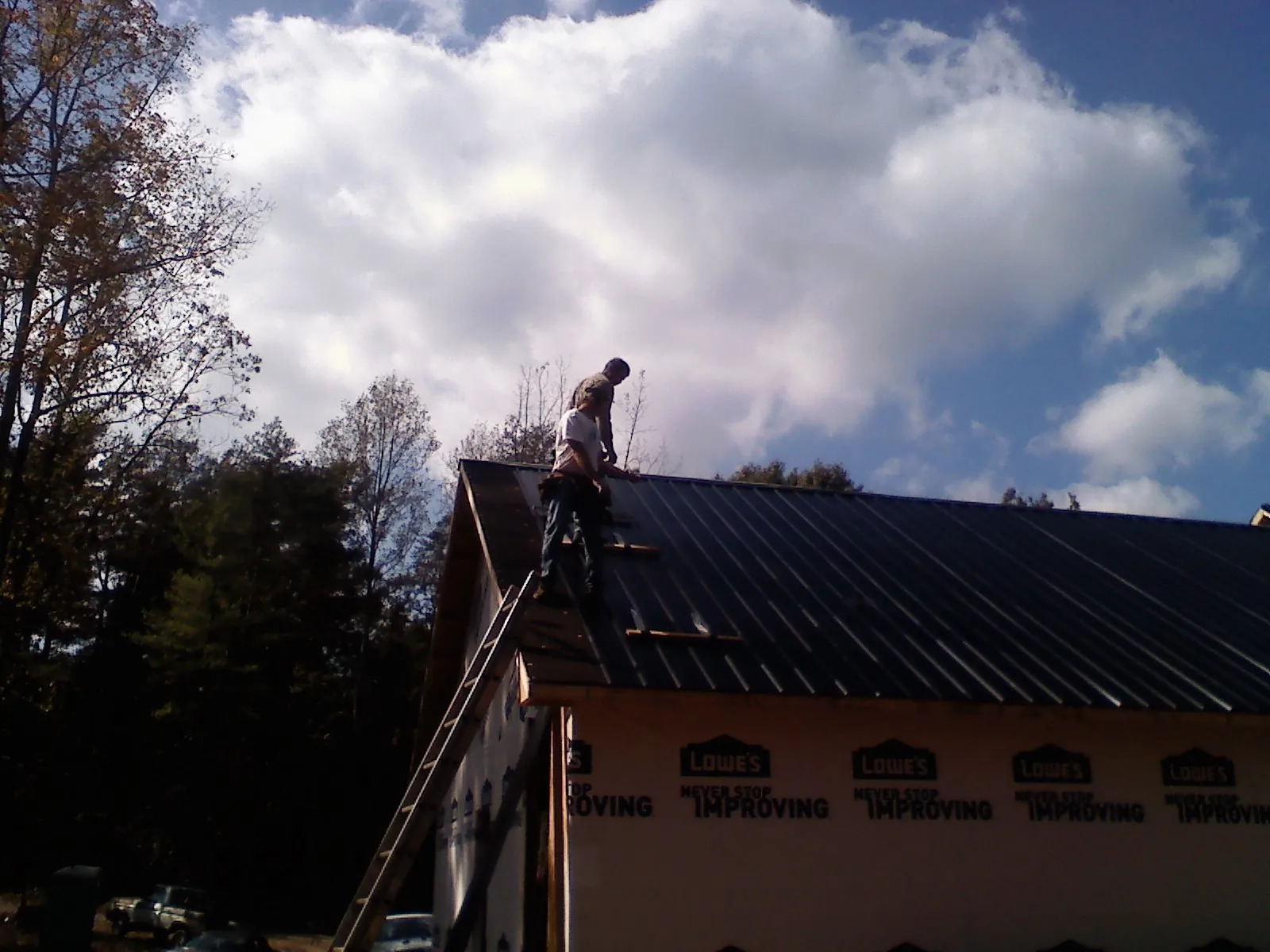 Roofer fastening dark metal panels high against a cloudy sky, from a Roof Inspection job in Omega
