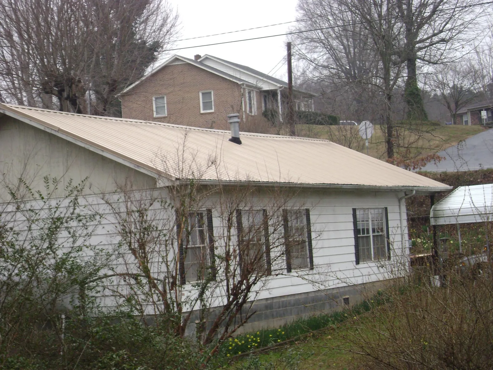 Tan metal roof on a white sided house set into a hillside — Commercial Roofing by Roofing Brothers in Omega