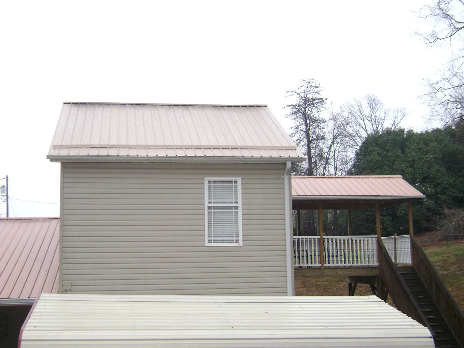 Tan metal roofs on a two story addition and attached porch, from a Roof Replacement job in Omega